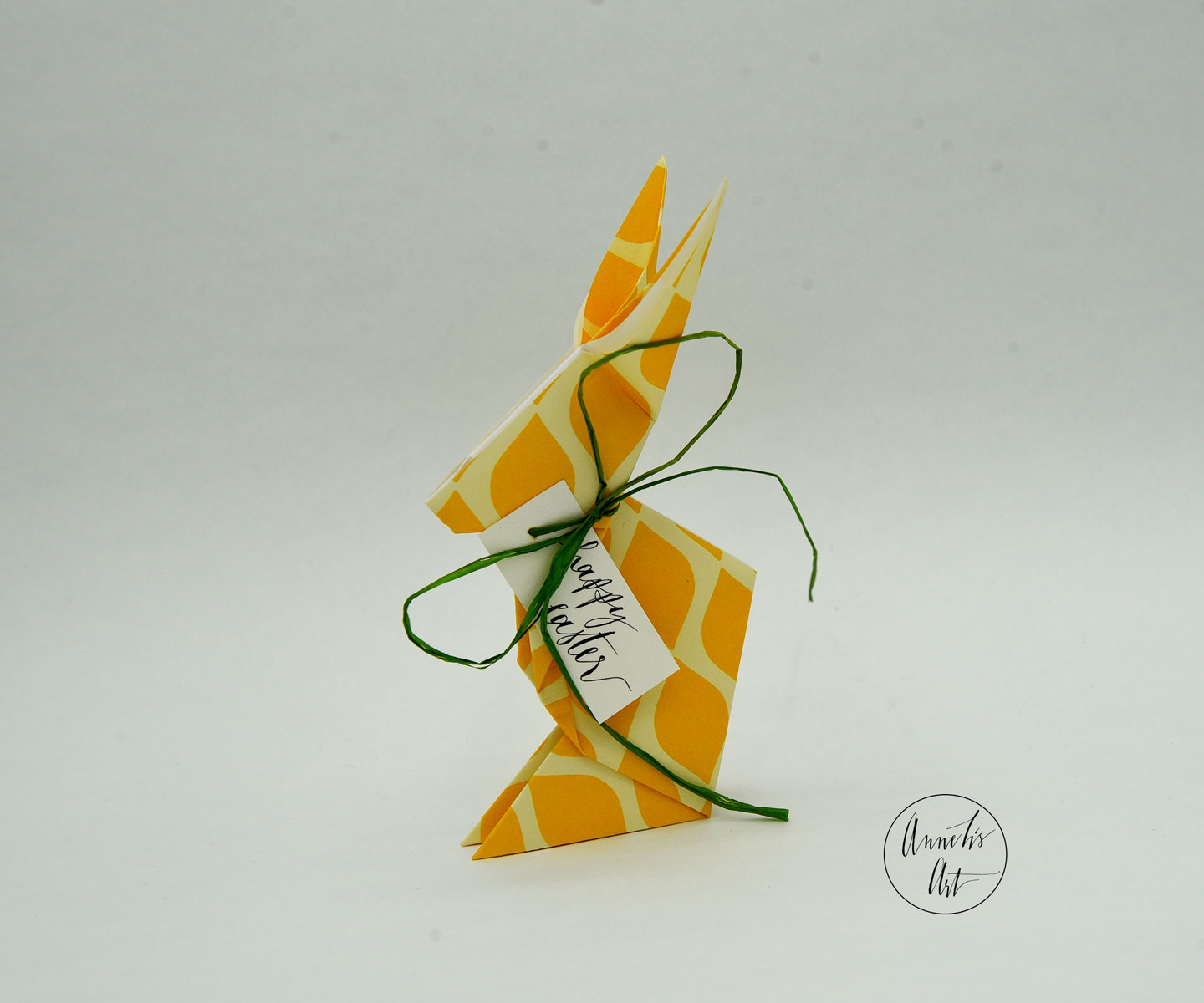 Gelbgemusterter Origami Osterhase mit grünem Band und Schriftzug